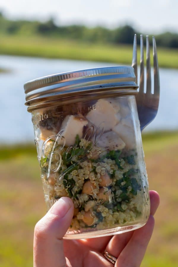 chickpea quinoa salad with turnip greens and grilled chicken on-the-go in a mason jar outside by a lake.