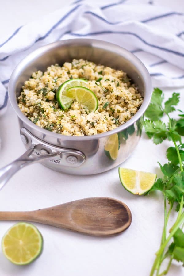 Cilantro lime quinoa in a small sauce pot with a wooden spoon and lime garnishes.