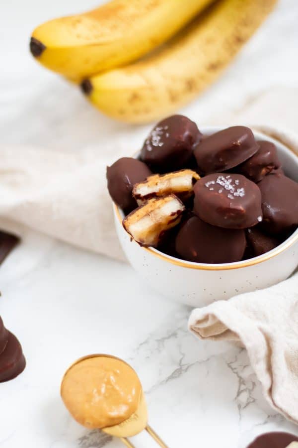 A small bowl filled with frozen banana bites with peanut butter and covered in chocolate.