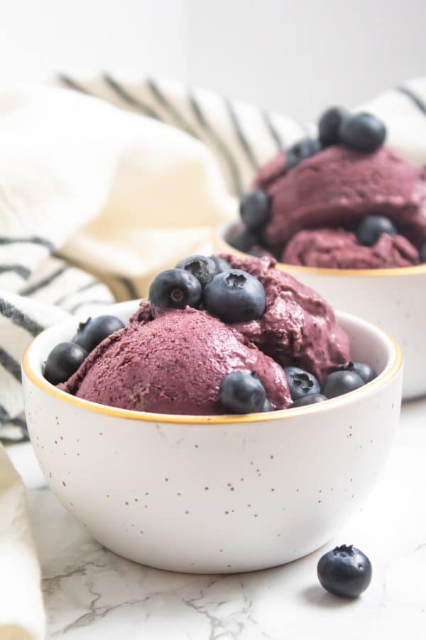 white bowl with gold trim and gold flecks full of a beautifully purple blueberry avocado nice cream and fresh blueberries