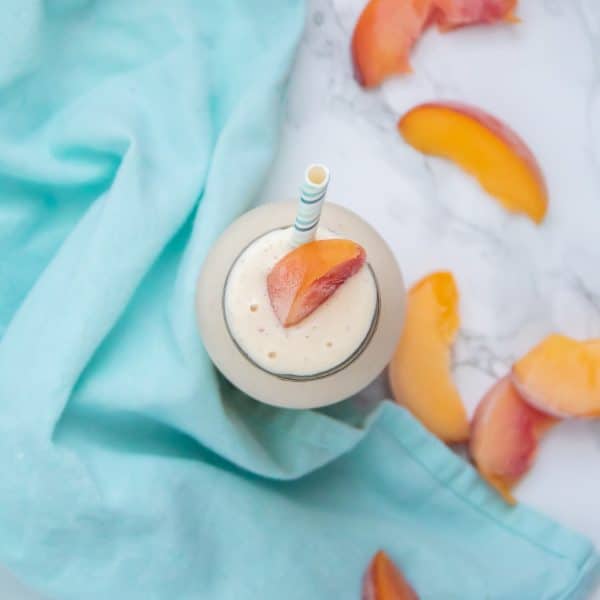 overhead shot of a peach garnish and banana peach smoothie in a glass jar with a blue cloth next to it.