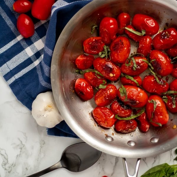 skillet with blistered tomatoes on a white and navy towel.