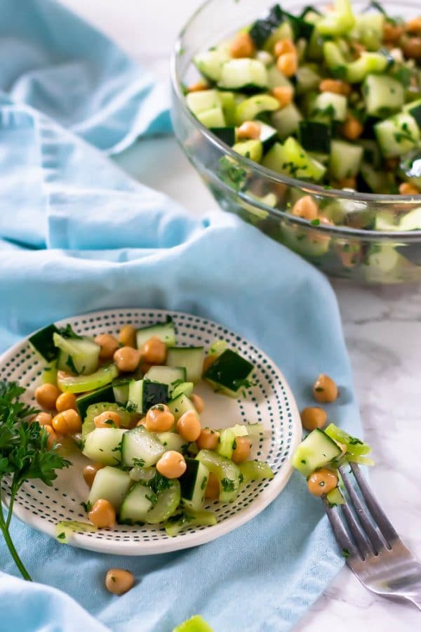 A small plate with cucumber chickpea salad with a glass bowl of the whole recipe in the background.