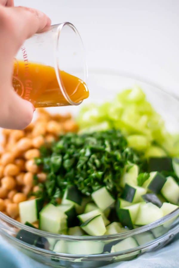 Pouring a simple red wine vinaigrette over the ingredients for cucumber chickpea salad.