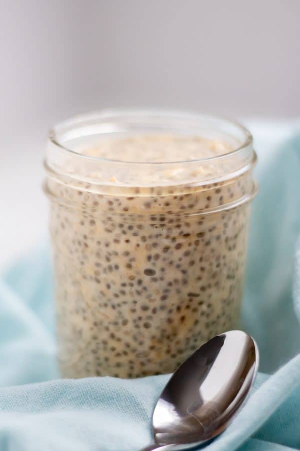 side view of a small mason jar full of creamy tan overnight oats studded wth chia seeds on a light aqua towel