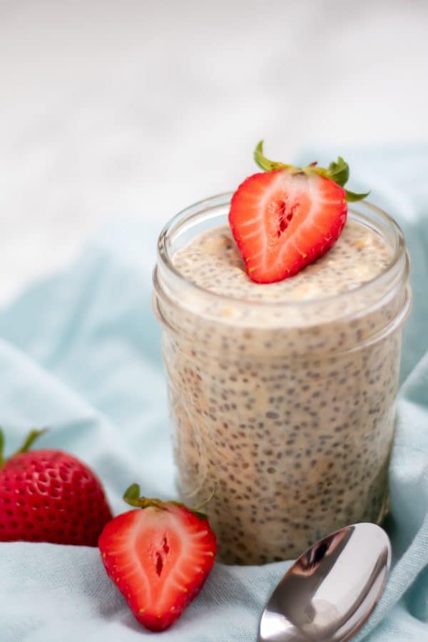 creamy pale tan overnight orange oats in a mason jar accented with halved strawberries