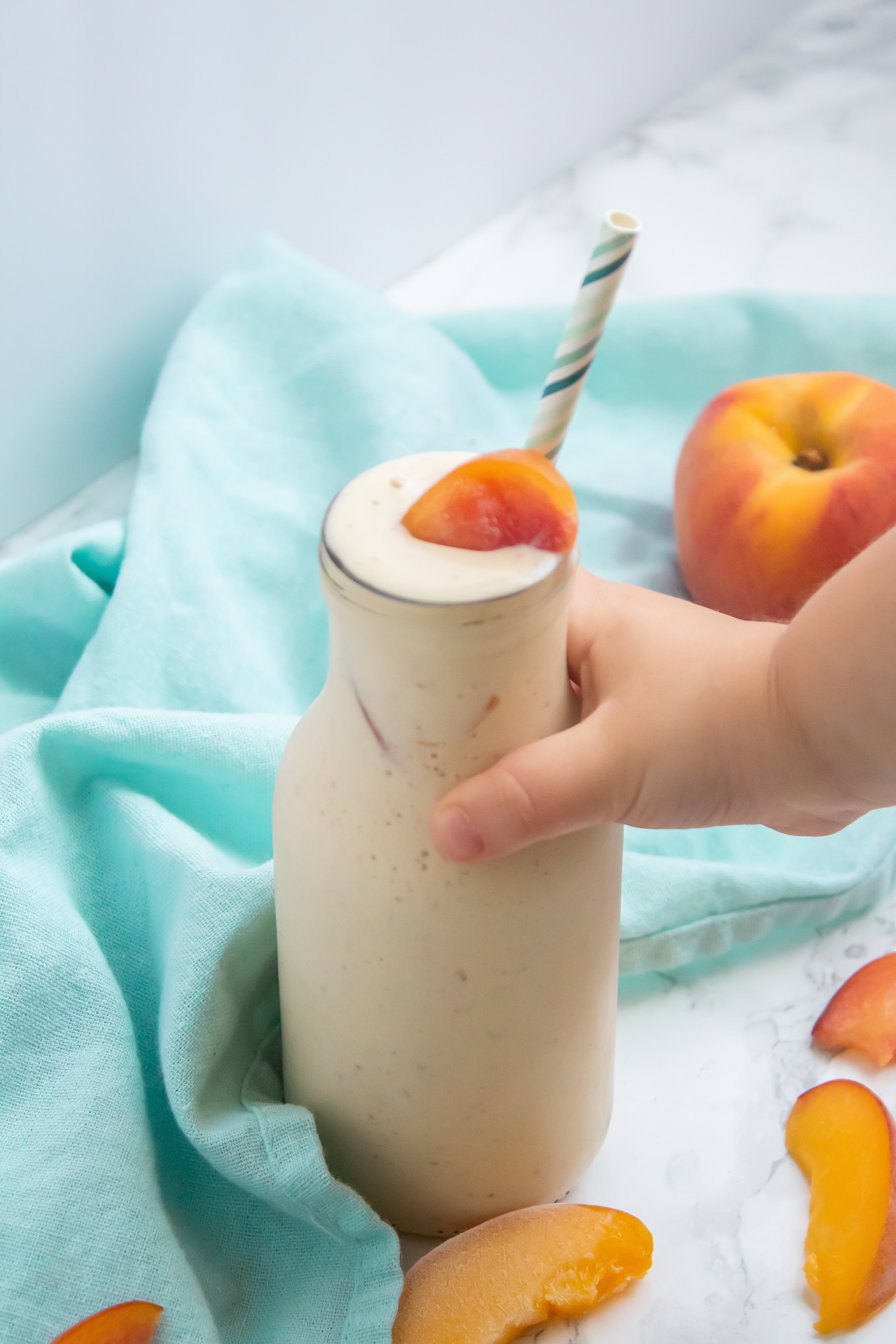 A small child's hand reaching for a glass of creamy banana peach smoothie.