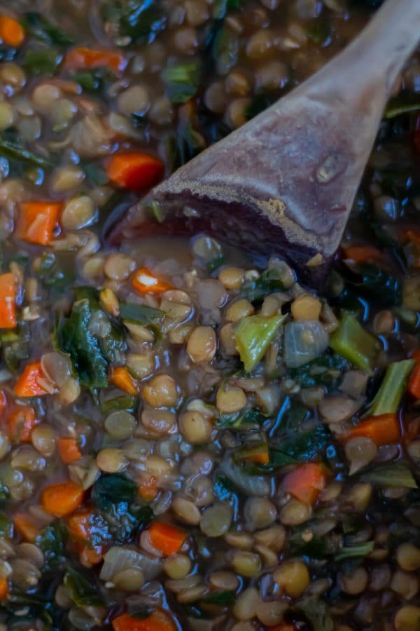 Close up of a wooden spoon in lentil stew specked witht turnip greens and carrots