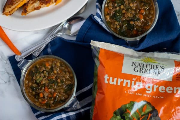 Two antique glass bowls of lentil stew on a blue towel with a bag of Nature's Greens turnip greens, featured in the stew