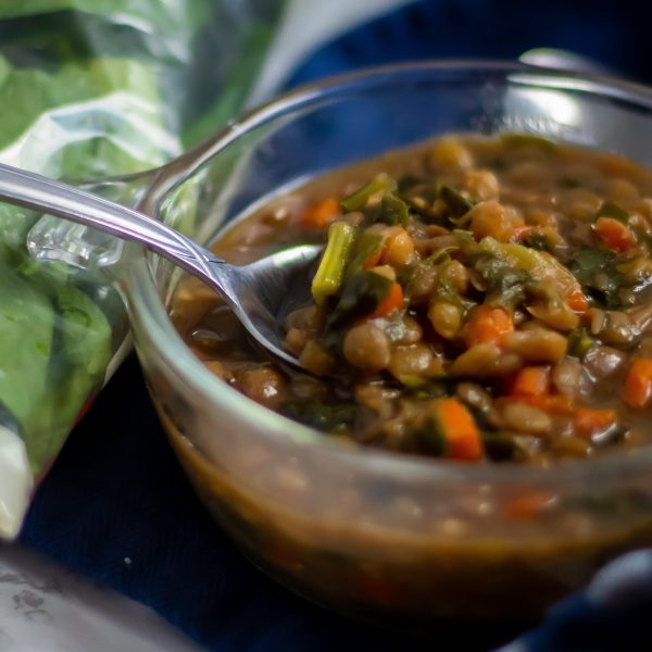 A spoon scooping a bite from a glass bowl of lentil stew