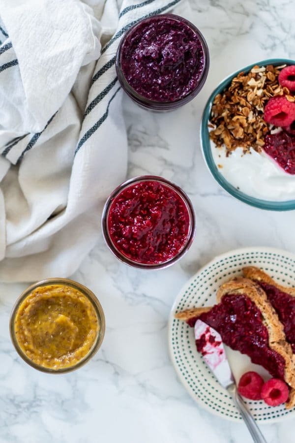 purple, red, and yellow chia jams next to a yogurt parfait and toast