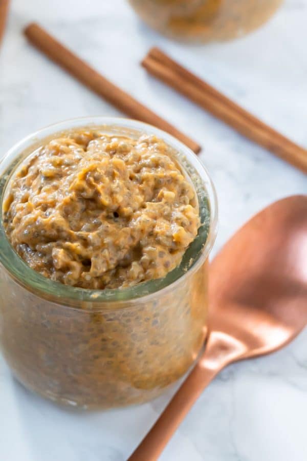 a copper spoon next to a small glass jar of pumpkin chia pudding