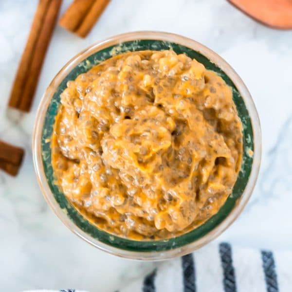 overhead shot of pumpkin chia pudding with cinnamon sticks next to the glass container on a marble surface.