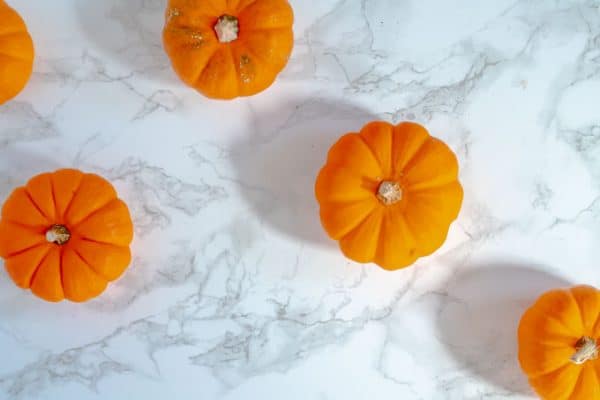 mini pumpkins and their shadows on a brightly lit marble background