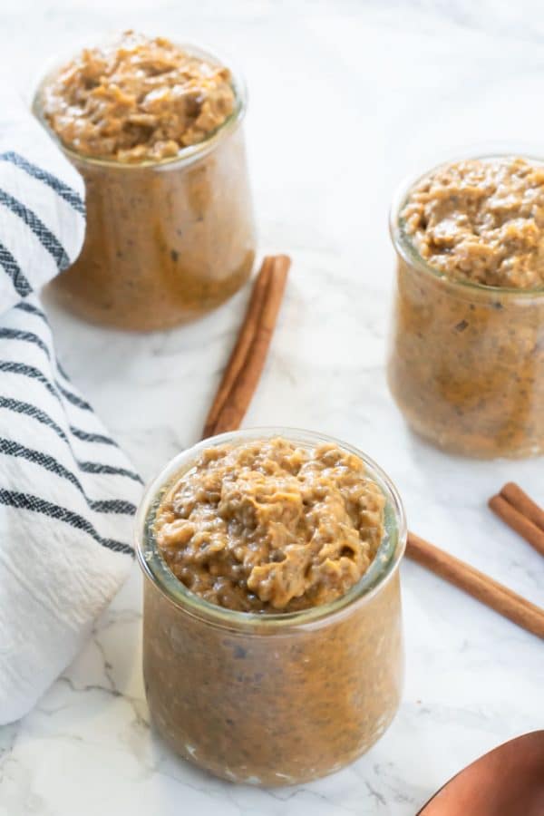 soft orange pumpkin chia pudding in small glass jars on a marble surface with cinnamon sticks