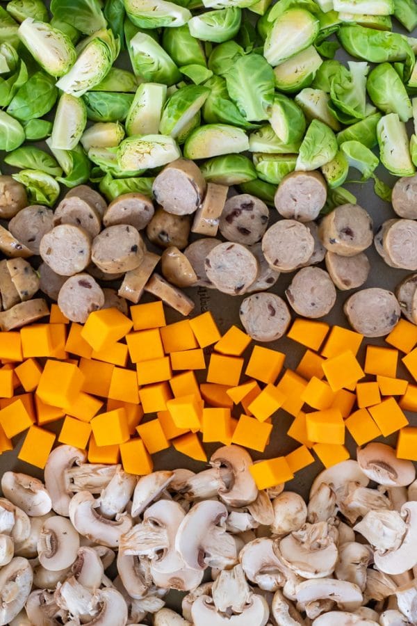 rows of brussels sprouts, chicken sausage, butternut squash, and mushrooms on a sheet pan ready to be roasted