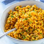 An ivory rustic, ceramic bowl with spiral shaped pasta tossed in pumpkin pasta sauce and garnished with parsley.