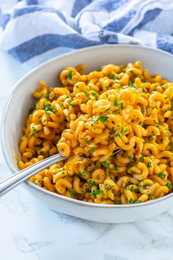 An ivory rustic, ceramic bowl with spiral shaped pasta tossed in pumpkin pasta sauce and garnished with parsley.