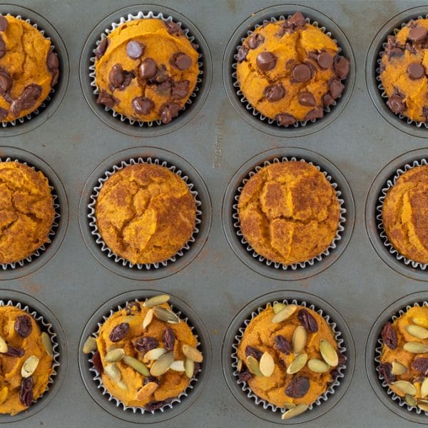 pumpkin muffins in a silver pan - the top row with chocolate chips, the middle row with cinnamon, and the bottom row with raisins and pumpkin seeds.