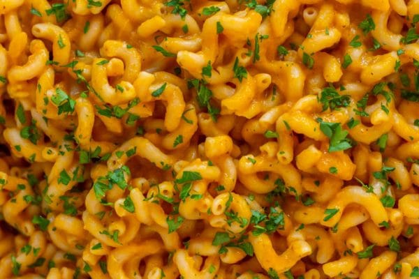 An up-close shot of spiral-shaped pasta tossed in pumpkin pasta sauce garnished with green parsley.