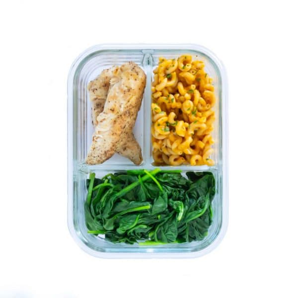 A 3-compartment glass meal prep container featuring pumpkin pasta, grilled chicken tenderloins, and steamed spinach.