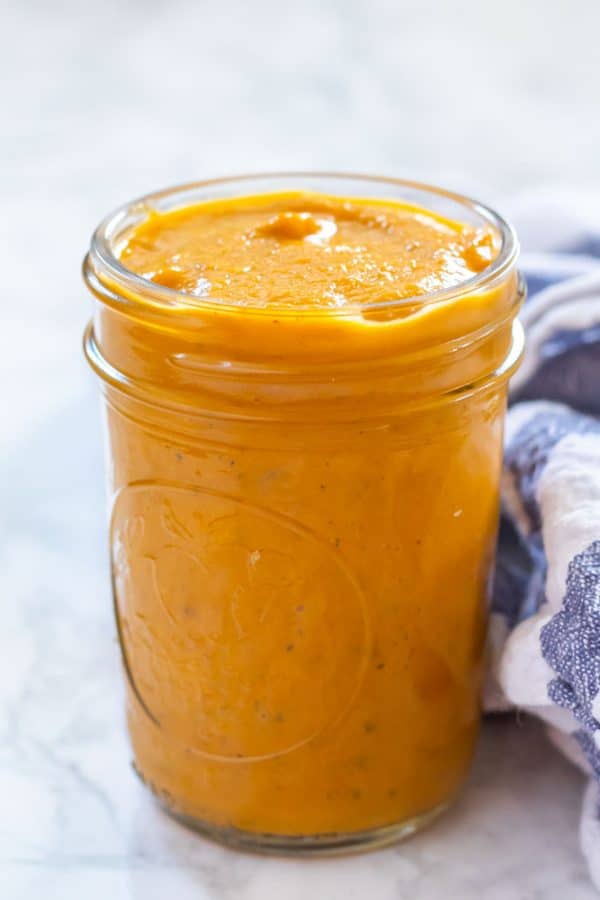 A glass jar of pumpkin pasta sauce on a marble surface against a white and blue broad striped kitchen towel.