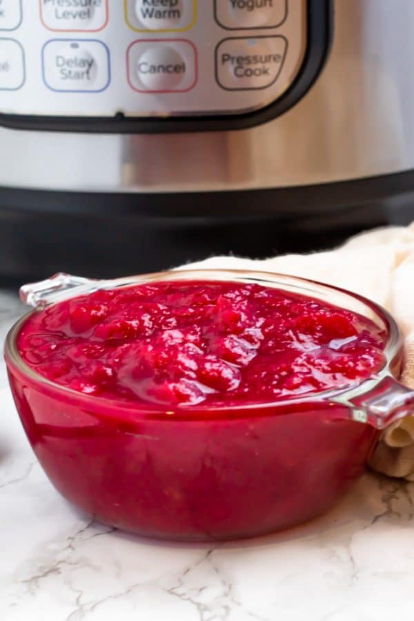 A small glass bowl of cranberry sauce with the Instant Pot in the background.