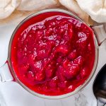 An overhead shot of a glass bowl of Instant Pot cranberry sauce with a black metal spoon and linen cloth.