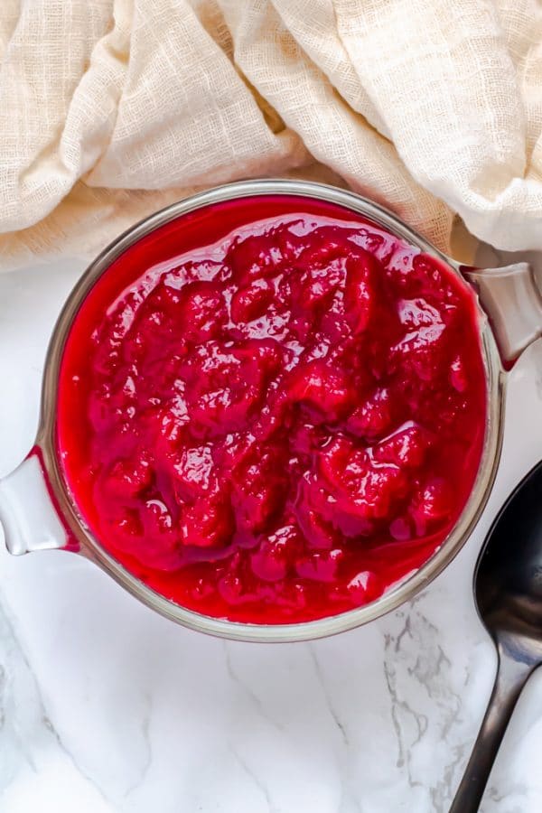 An overhead shot of a glass bowl of Instant Pot cranberry sauce with a black metal spoon and linen cloth.