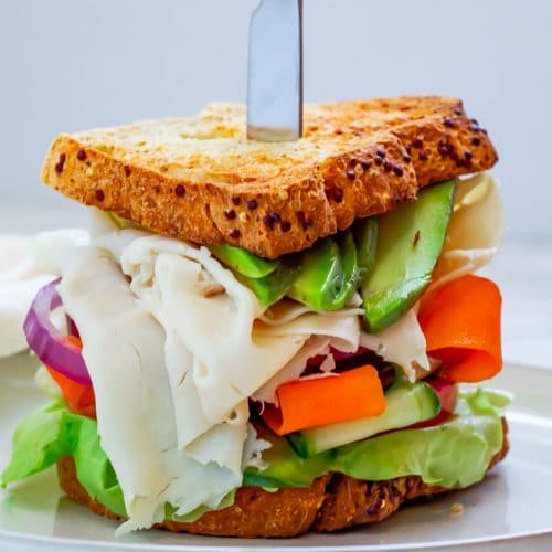 turkey avocado sandwich on whole grain bread loaded with veggies on a white ceramic plate