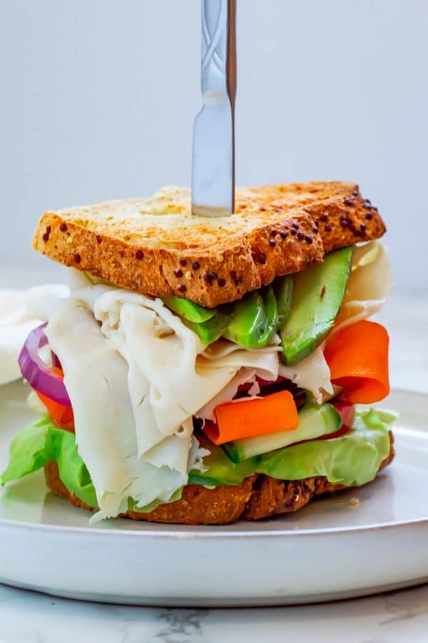 turkey avocado sandwich on whole grain bread loaded with veggies on a white ceramic plate