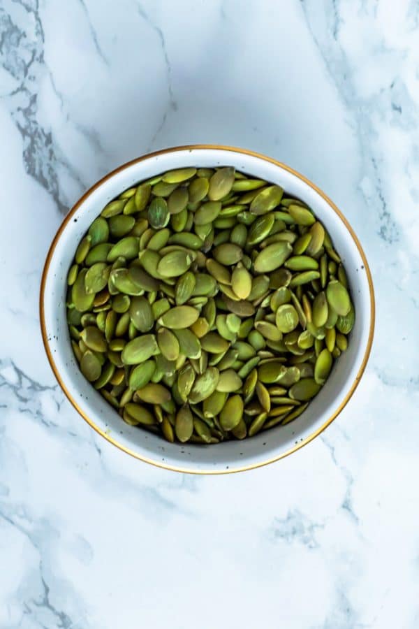 Pumpkin seeds in a white bowl on a marble surface.