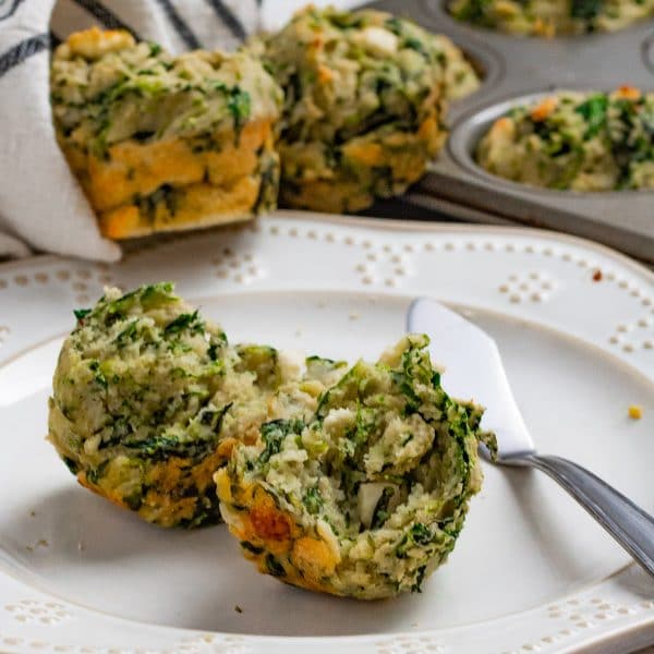 a spinach and feta muffin broken in half on a cream plate.