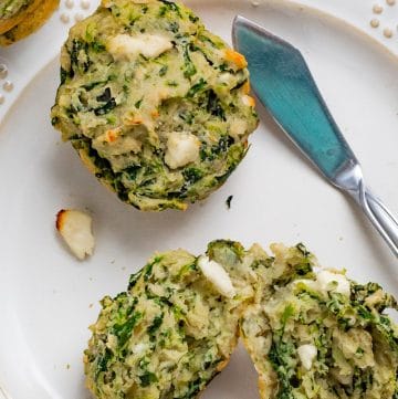 two spinach and feta muffins on a white plate, one sliced in half.