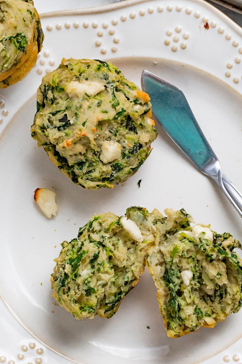 two spinach and feta muffins on a white plate, one sliced in half.