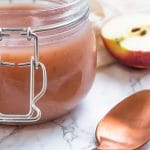 A small glass tub of rosy colored, smooth homemade applesauce.