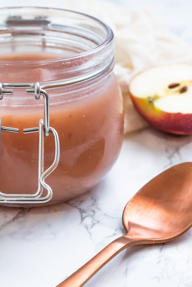 A small glass tub of rosy colored, smooth homemade applesauce.