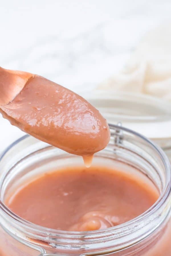 A copper spoon of applesauce over a jar.