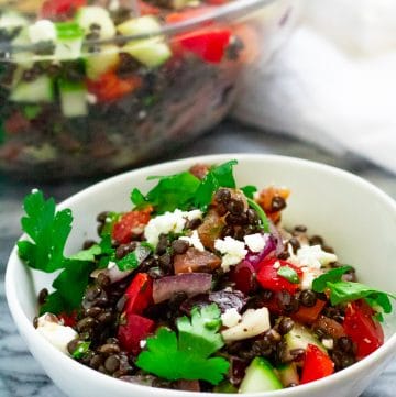 A small white bowl of greek lentil salad garnished with feta cheese and parsley.