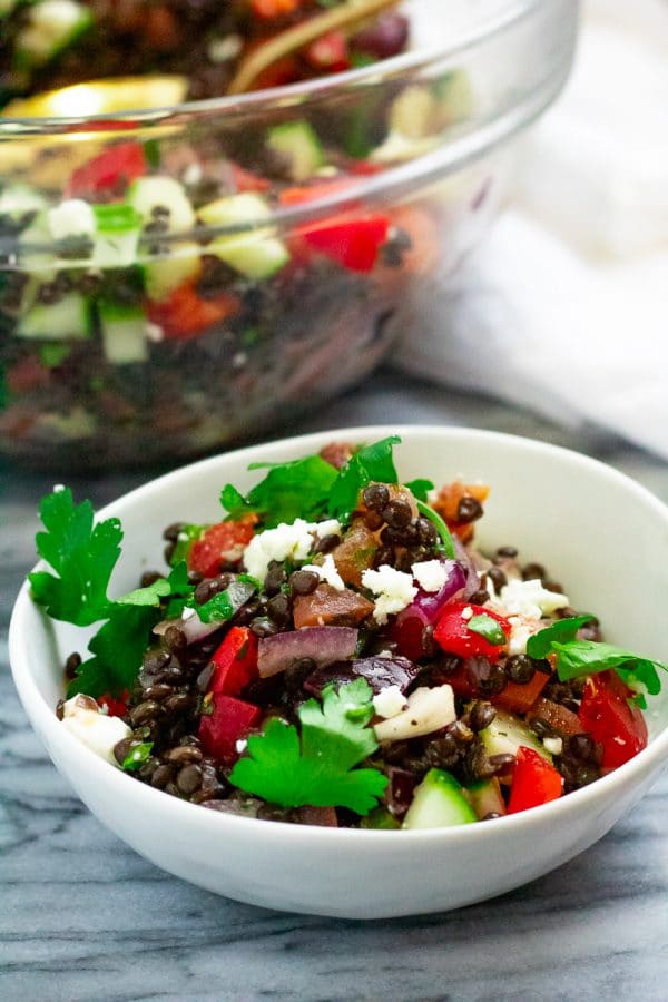 A small white bowl of greek lentil salad garnished with feta cheese and parsley.