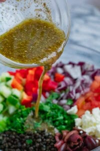 pouring dressing over greek lentil salad