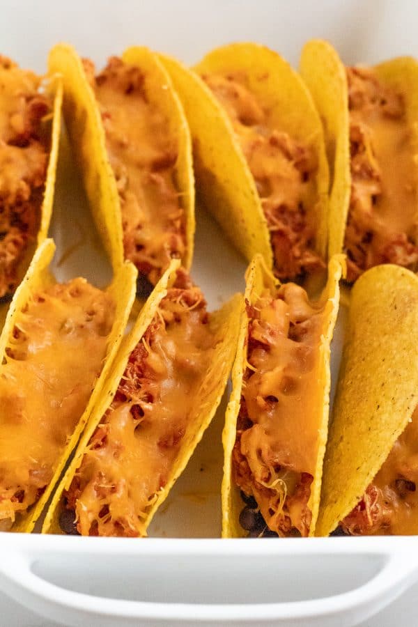 cheesy baked chicken tacos standing upright in a white baking dish