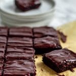 sliced chocolate avocado brownies on brown parchment paper with fudgy ganache frosting