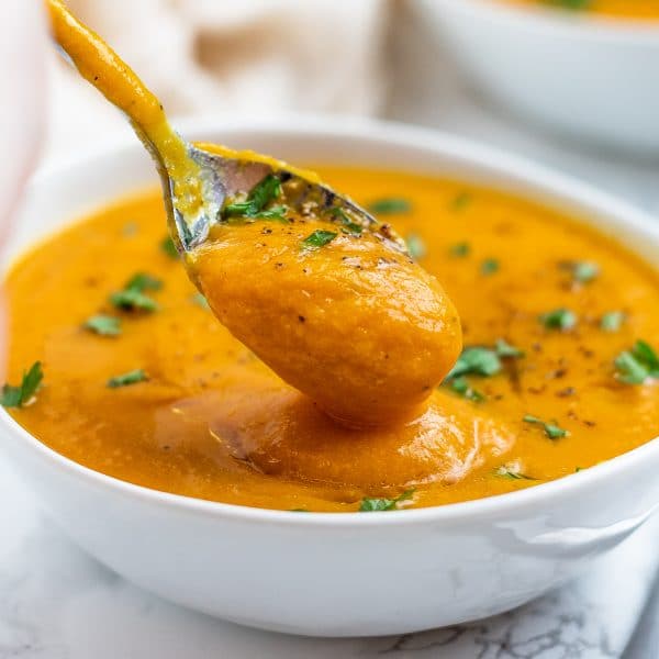 golden orange-colored soup in a white bowl with a silver spoon taking a spoonful of creamy smooth carrot lentil soup.