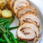 slices of chicken cordon bleu, crispy golden brown spirals of chicken, ham, and cheese, on a plate next to green beans and baby potatoes.