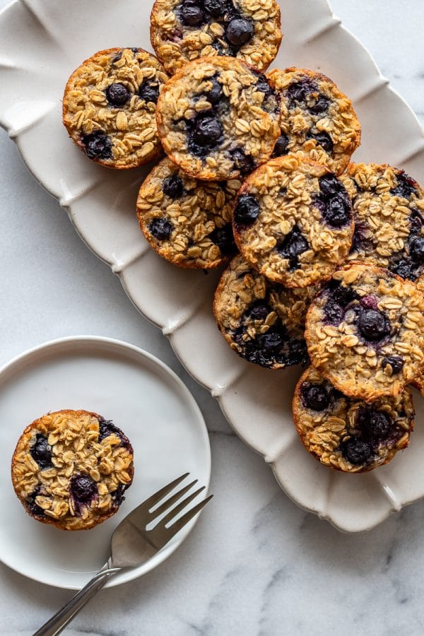 baked oatmeal cups with blueberries on a ceramic plattern with one on a small plate with a fork