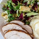 slices of air fryer turkey breast on a plate with a kale salad and mashed potatoes
