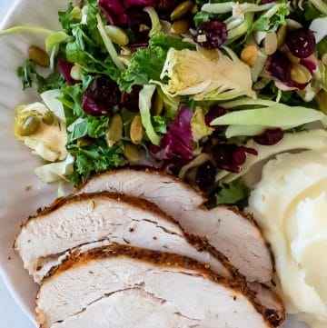 slices of air fryer turkey breast on a plate with a kale salad and mashed potatoes