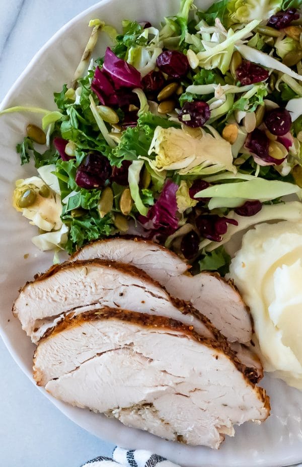 slices of air fryer turkey breast on a plate with a kale salad and mashed potatoes
