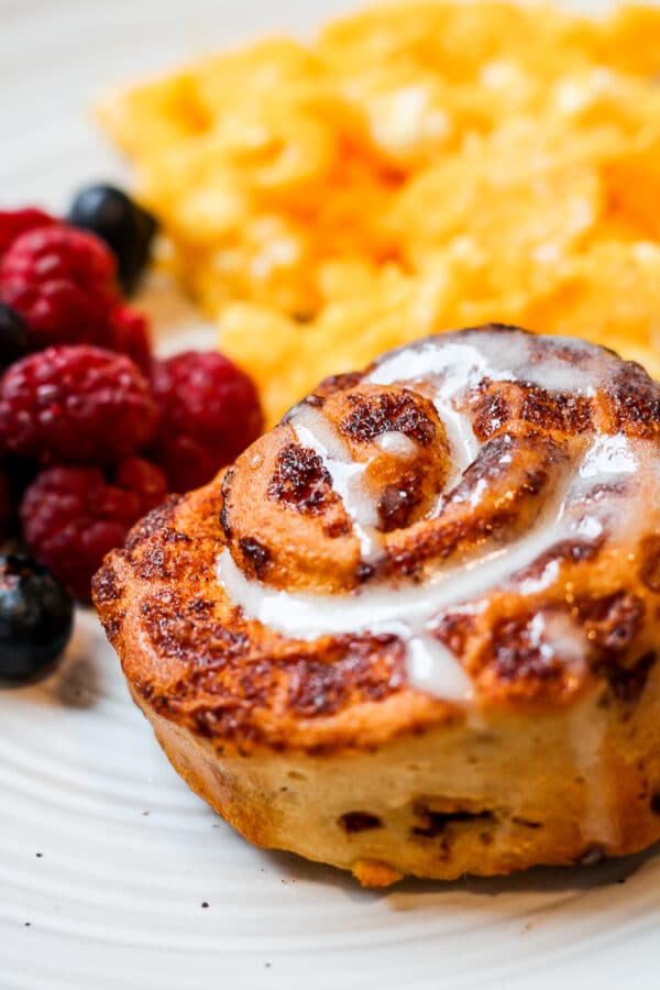 an air fryer cinnamon roll on a plate with scrambled eggs and fresh berries